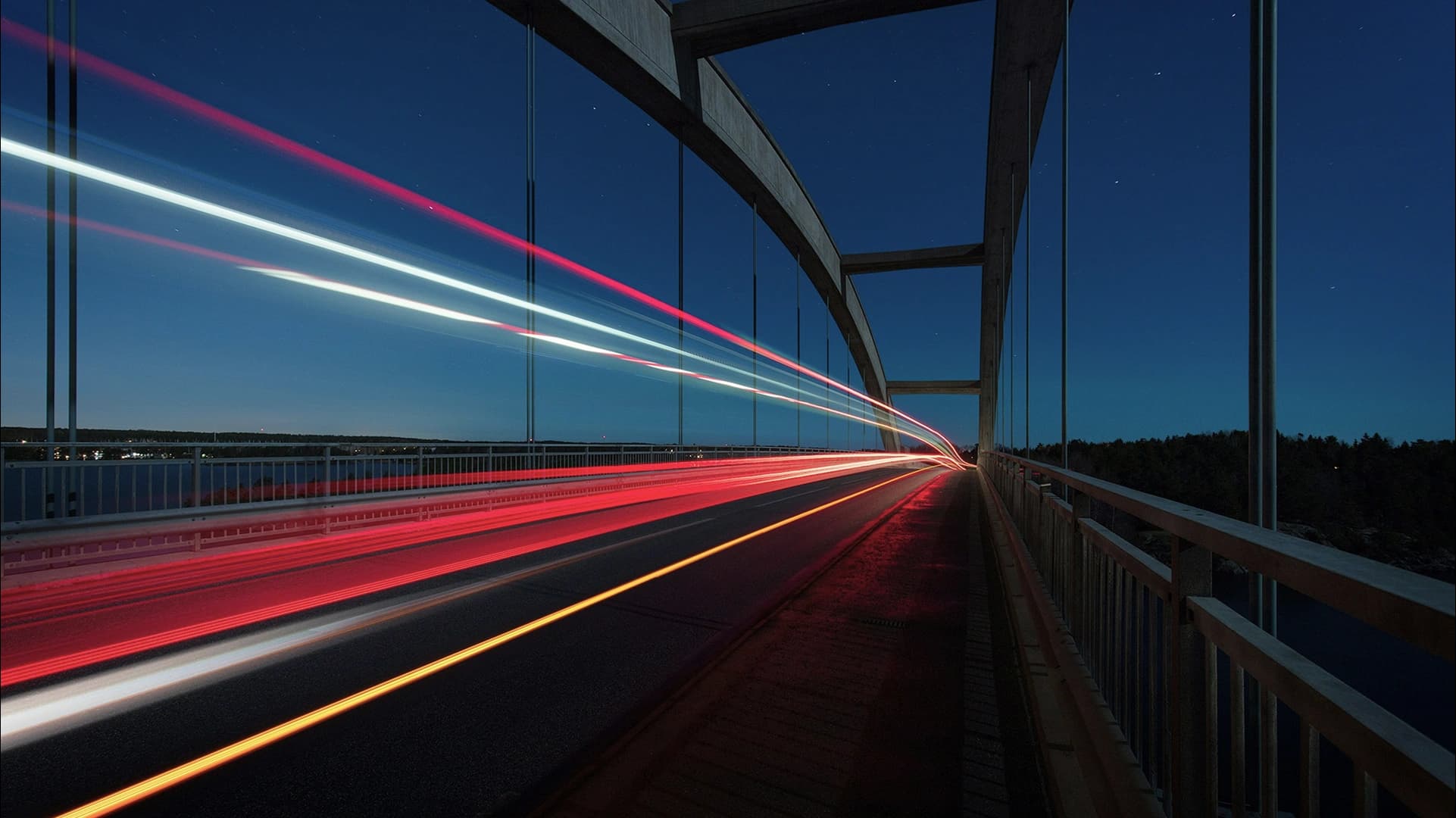 Car light trails streaking across a bridge under a clear night sky.